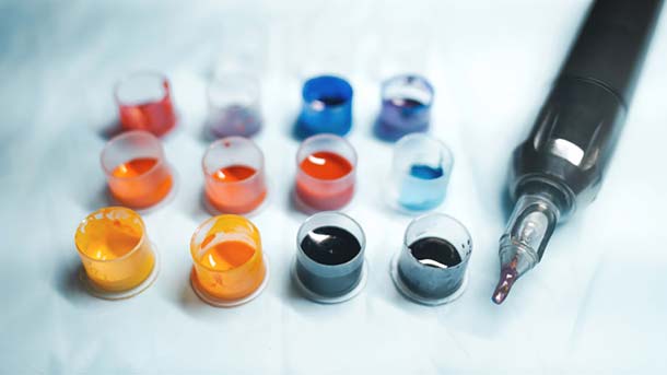 Des pots de tatouage et une machine à tatouer se trouvent sur une table blanche. Les encres de tatouage ne nécessitent aucune approbation au Scheiz.