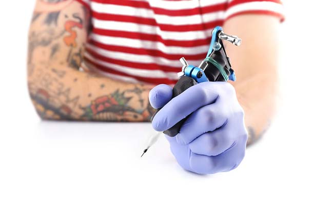 Un tatoueur tient une machine à tatouer dans la caméra avec une main. Il porte des gants stériles.