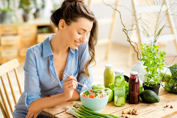 Eine zufriedene Frau geniesst in einen frischen Salat, umringt von frischen Zutaten für eine gesunde Ernährung.