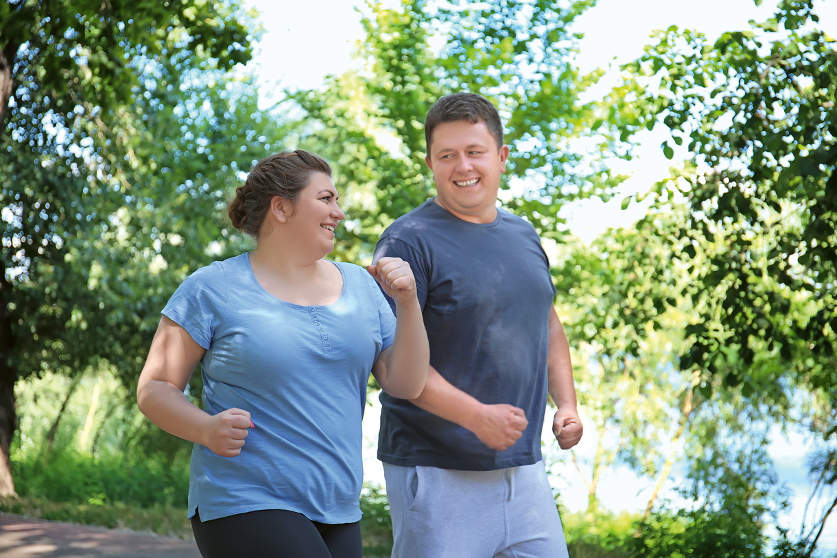 Ein übergewichtiges Paar joggt motiviert durch einen grünen Park.