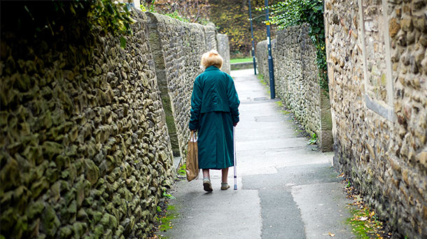 Eine alte Dame spaziert alleine einen Weg entlang. 