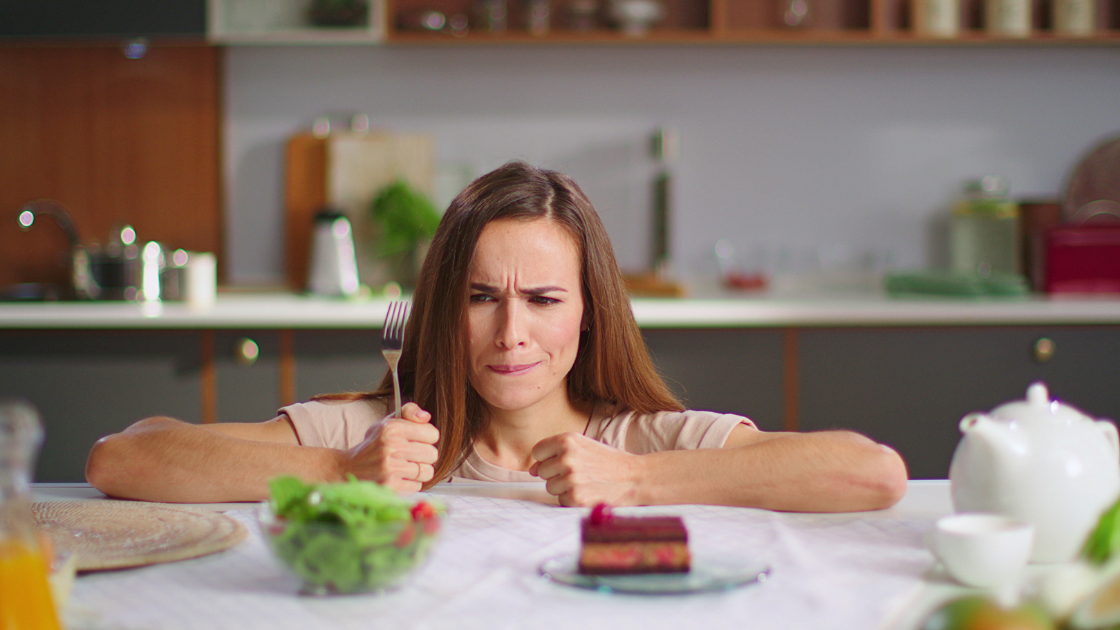 Eine Frau hadert mit dem Entscheid was sie essen soll. Salat oder Torte, beides steht vor im auf dem Tisch.
