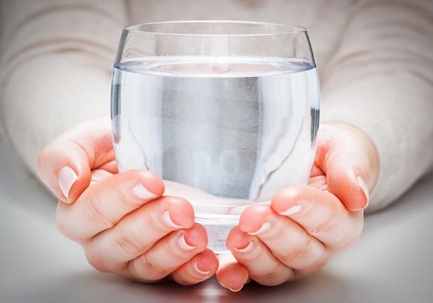 Bildbeschreibung: Eine Frau hält ein volles Wasserglas in beiden Händen. Wasser ist für viele Stoffwechselprozesse im Körper unerlässlich. 