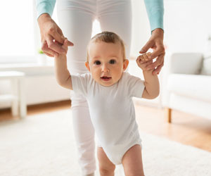 Eine Mutter hält ihr Baby an den Händen und es macht die ersten Schritte mit Unterstützung.