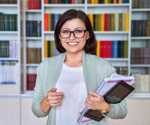 Eine zielstrebige Frau im mittleren Alter steht vor einem bunt bestückten Bücherregal.