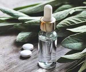 Glasfläschchen mit klarem Gel, zwei Tabletten und frischen Salbeiblättern auf Holz – symbolische Darstellung pflanzlicher, bioidentischer und synthetischer Unterstützungsmöglichkeiten in den Wechseljahren.