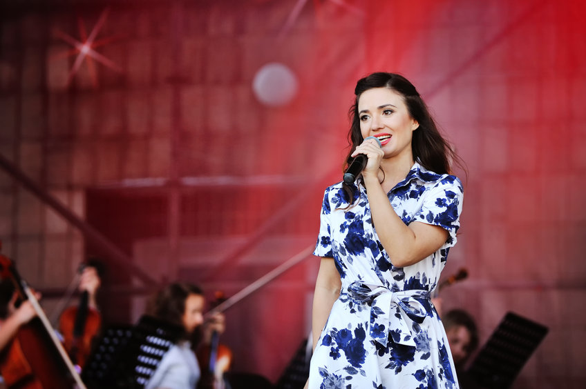 Eine Sängerin steht mit dem Mikrofon in der hand auf der Bühne.