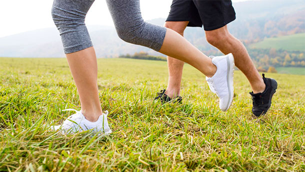 Zwei Personen joggen über eine Wiese. Im Bildausschnitt sind nur die Füsse bis zu den Knien zu sehen.