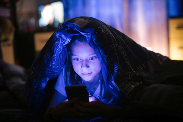 Ein Mädchen liegt unter der Decke und sieht im Dunkeln auf ihr Smartphone.