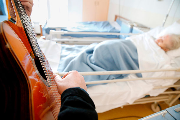 Jemand spielt Gitarre neben einem Patienten im Krankenhausbett.