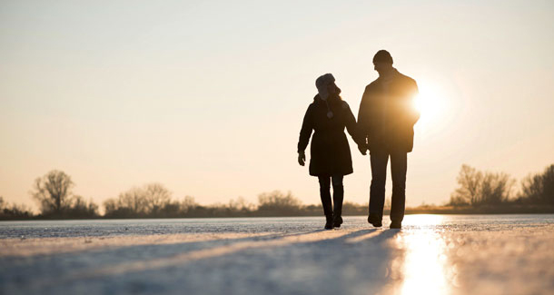 On peut voir un couple marcher dans un paysage enneigé. Le coucher de soleil colore déjà la scène d'un jaune chaud.