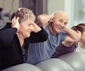 Eine Gruppe diverser Menschen trainiert im Fitnessraum den Rücken mit einem Gymnastikball.